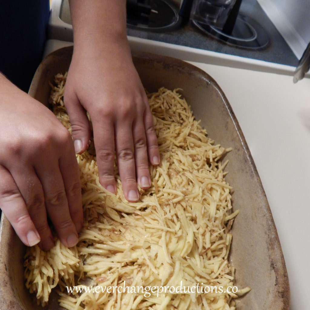 Step One of my favorite local recipe: shred potatoes and layer them in pan.