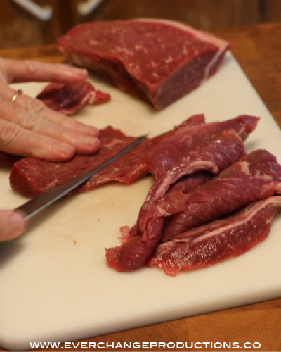 Trim off the fat and slice the round steak into 1/8 to 1/4 inch slices with the grain for chewy slices or against the grain for tender jerky.