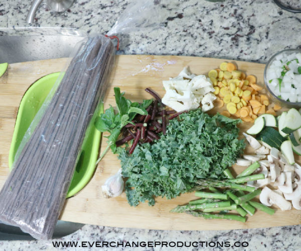 Ingredients for summer vegetable pasta include noodles, peppers, zucchini, mushrooms, asparagus, kale, green beans, garlic, carrots, and basil